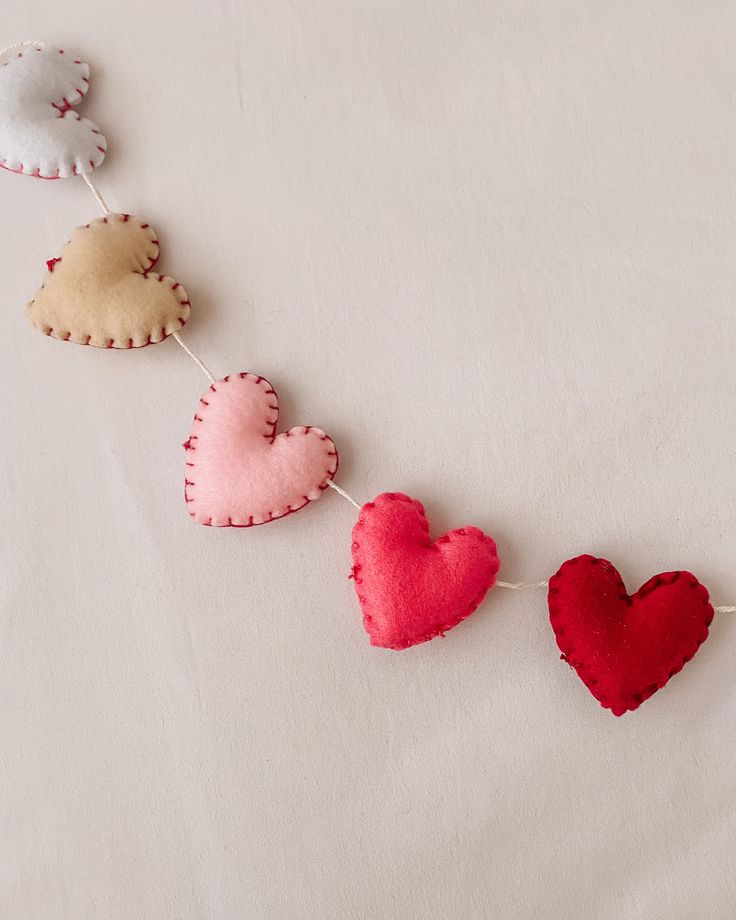 three felt hearts hanging from a string on a white sheet with red and pink heart shapes