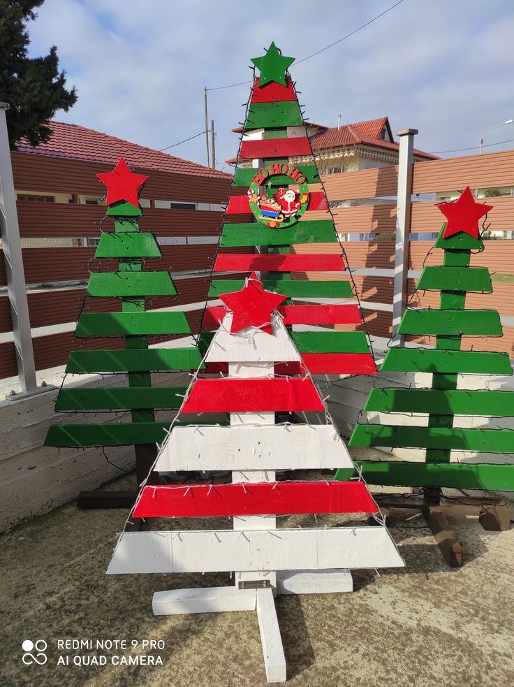 three wooden christmas trees sitting next to each other on top of a cement slab in front of a fence