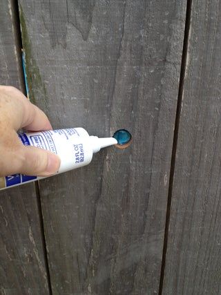 a hand holding a toothbrush near a wooden fence with blue and white paint on it