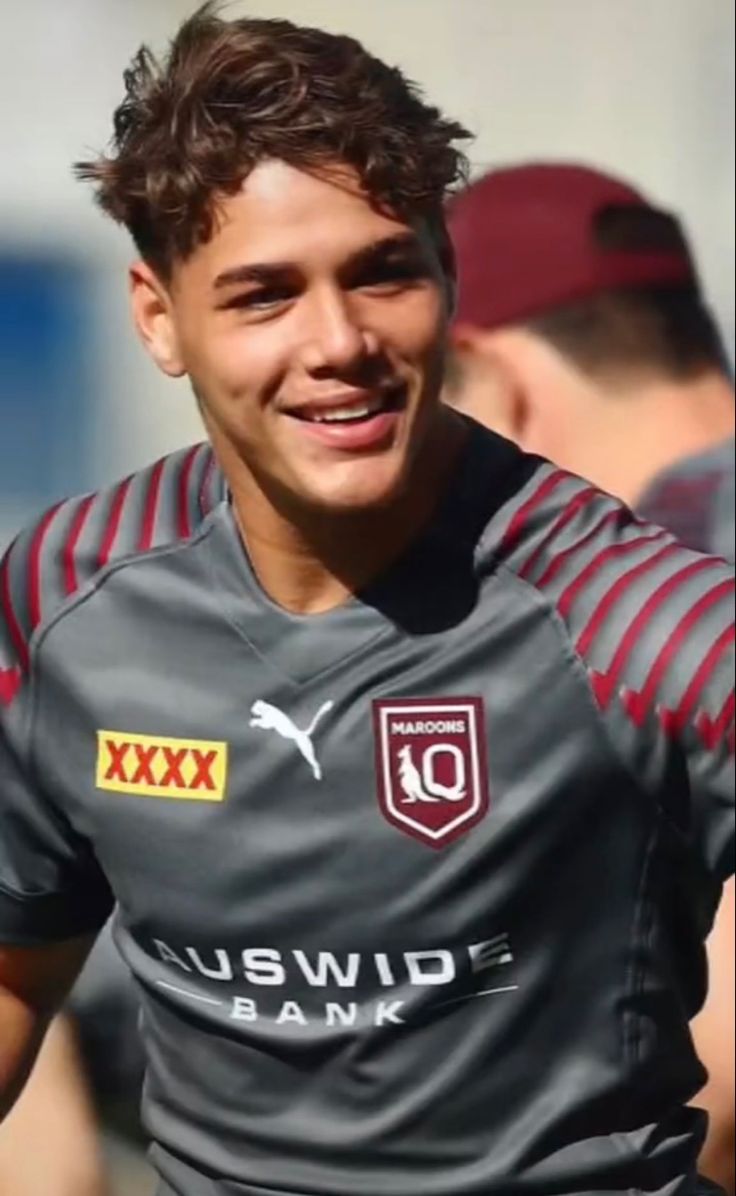 a young man is smiling and wearing a grey shirt with red stripes on it's sleeves