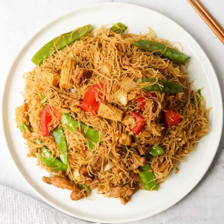 a white plate topped with noodles and veggies next to chopsticks on a table