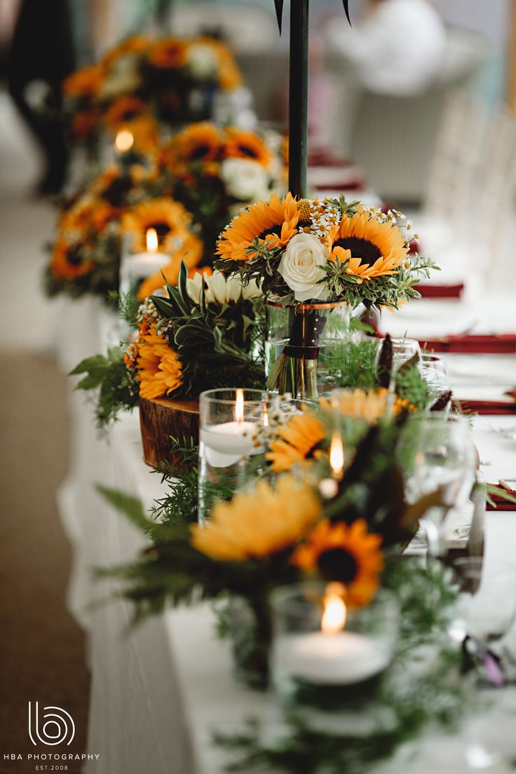 a long table with sunflowers and greenery on it, surrounded by candles