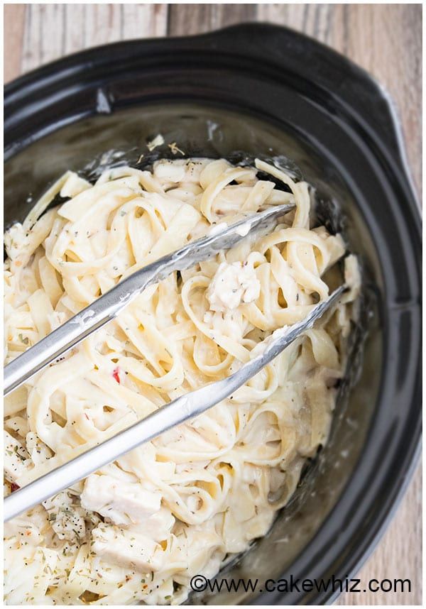 two tongs in a slow cooker filled with pasta