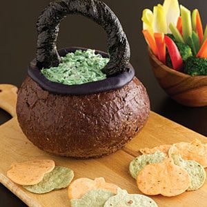 a bread bowl filled with dip and crackers on a cutting board next to flowers