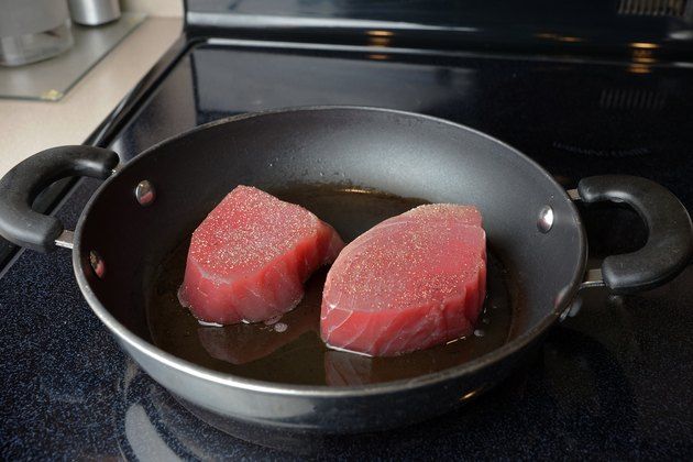 two pieces of raw meat cooking in a pan on the stove top next to an oven