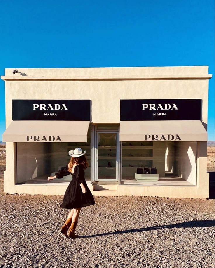 a woman in a black dress and white hat walking past a prada store