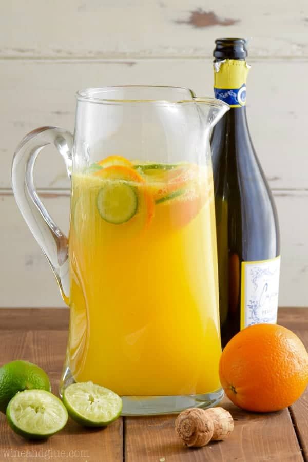 a pitcher filled with orange juice next to an orange and cucumber on a wooden table