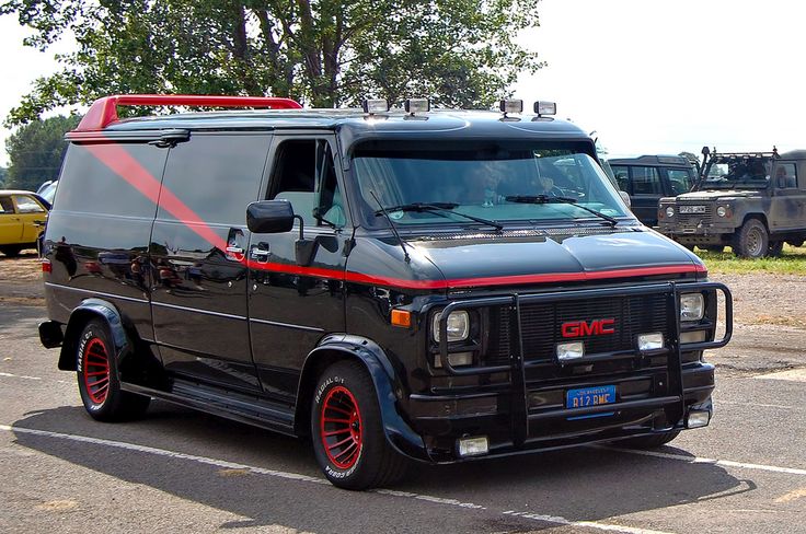 a black van parked in a parking lot next to other cars and trucks behind it