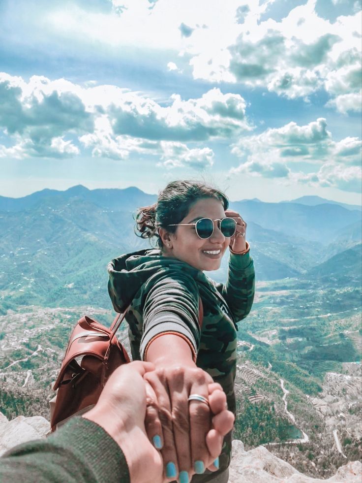 a woman holding the hand of a man on top of a mountain