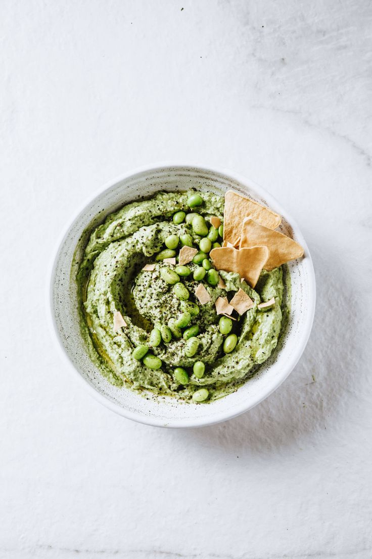 a white bowl filled with green food and a tortilla chip on top of it