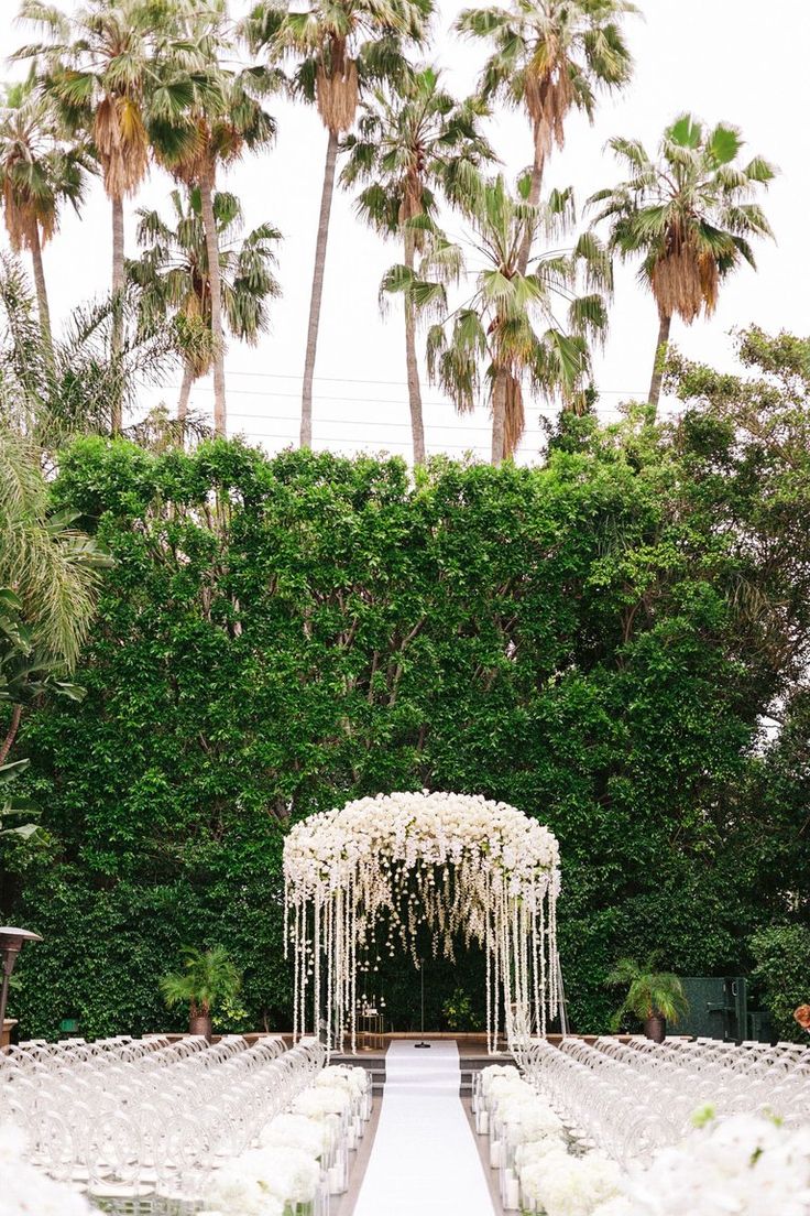 an outdoor ceremony setup with white flowers and greenery on the side, surrounded by palm trees