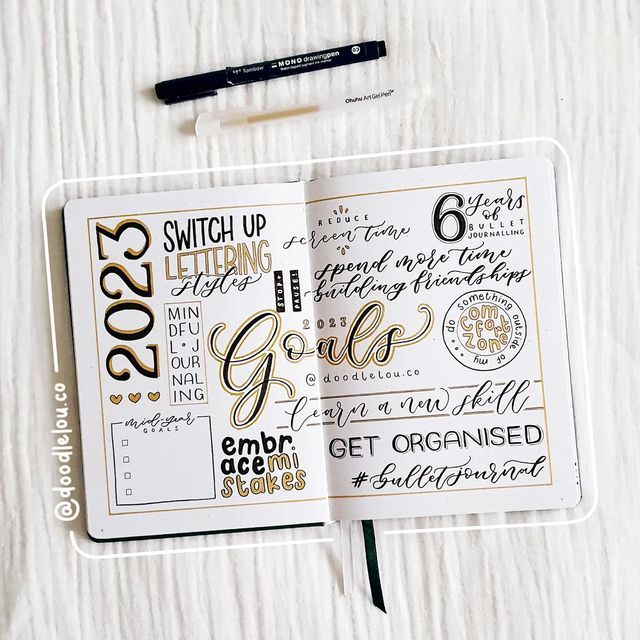 an open planner with gold lettering on it and a black pen laying next to it