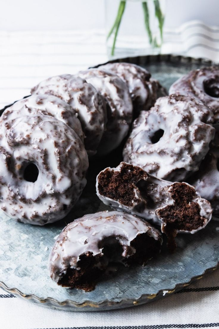 chocolate donuts with white frosting on a plate next to a vase filled with flowers