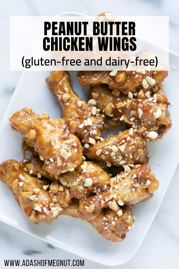 a white plate topped with chicken wings covered in peanut butter and sesame seed flakes