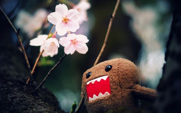 a stuffed animal is sitting on a tree branch with pink flowers in the back ground