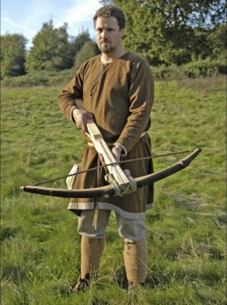 a man dressed in medieval clothing holding a bow and arrow while standing in a field