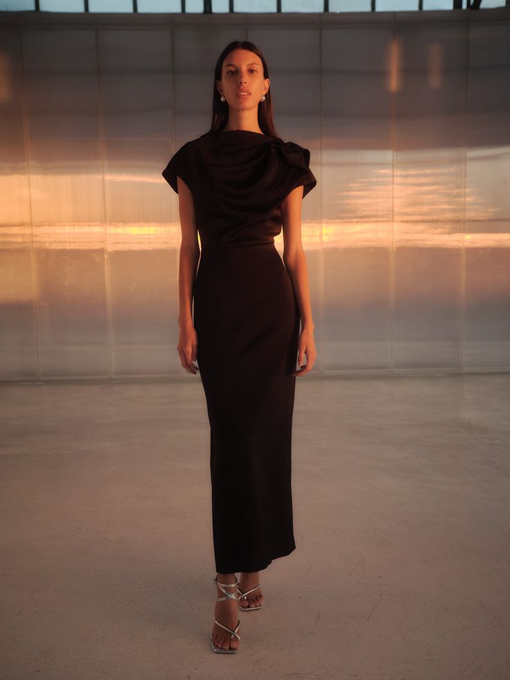 a woman standing in front of a wall wearing a black dress