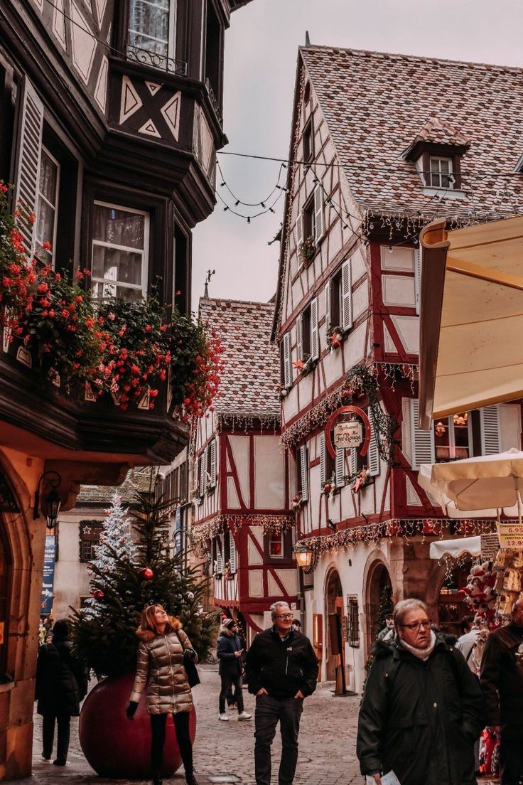 people are walking around in an old european town with christmas decorations on the buildings and trees