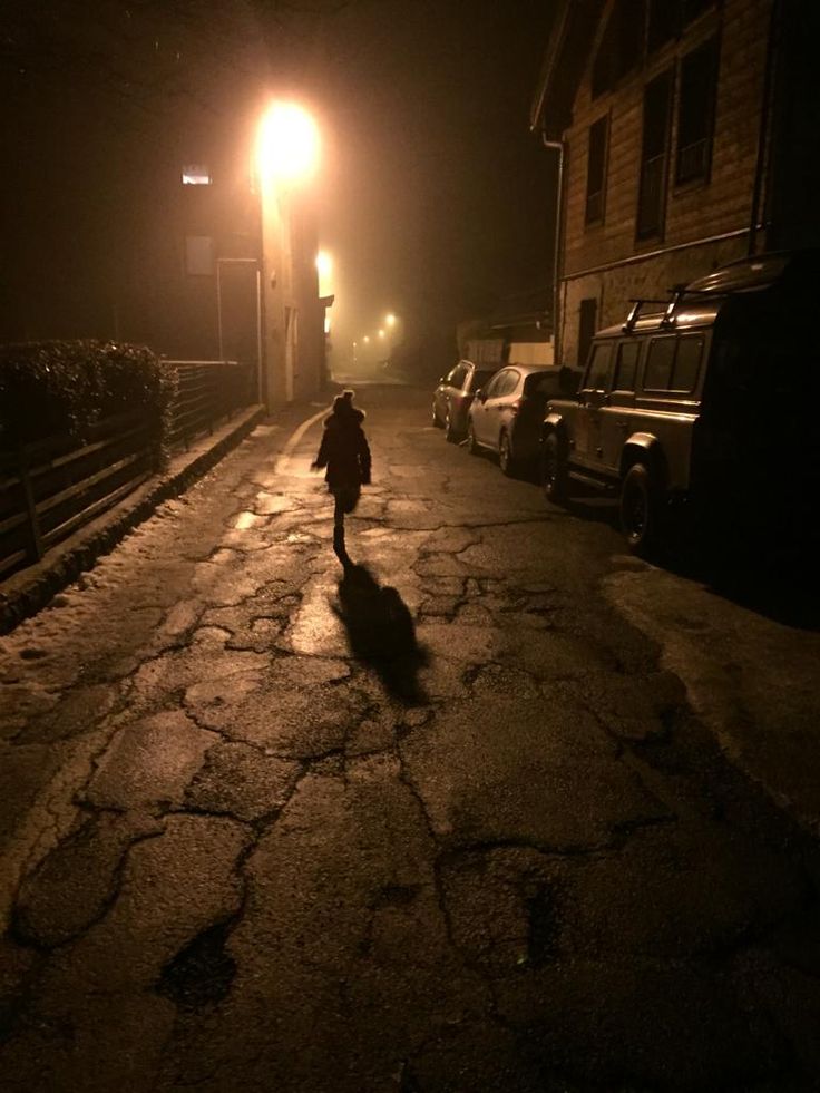 a person walking down a street at night in the dark with no one on it