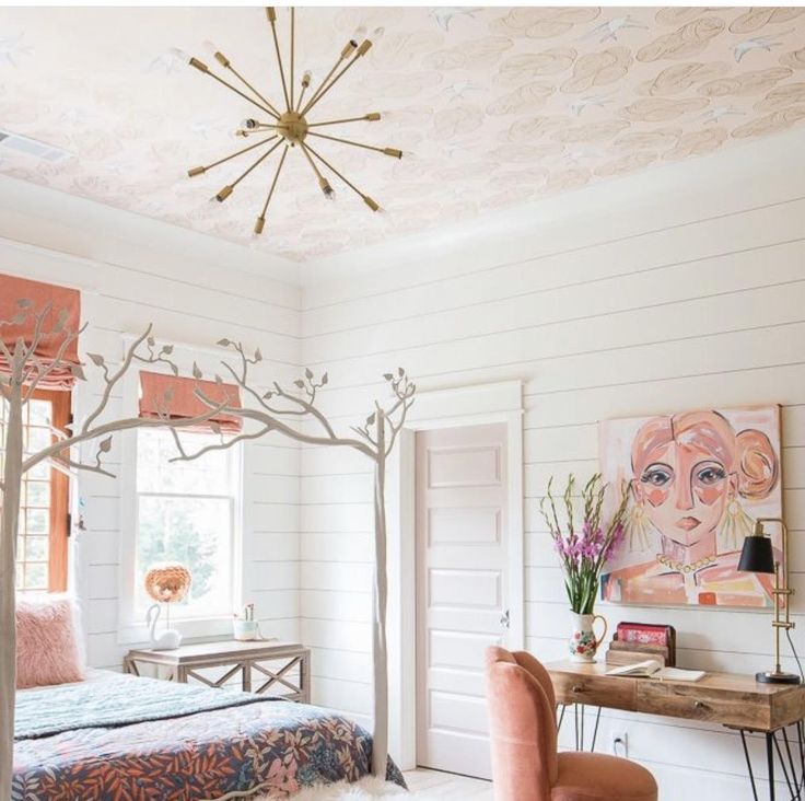 a bedroom decorated in pink and white with a bed, chair, desk and artwork