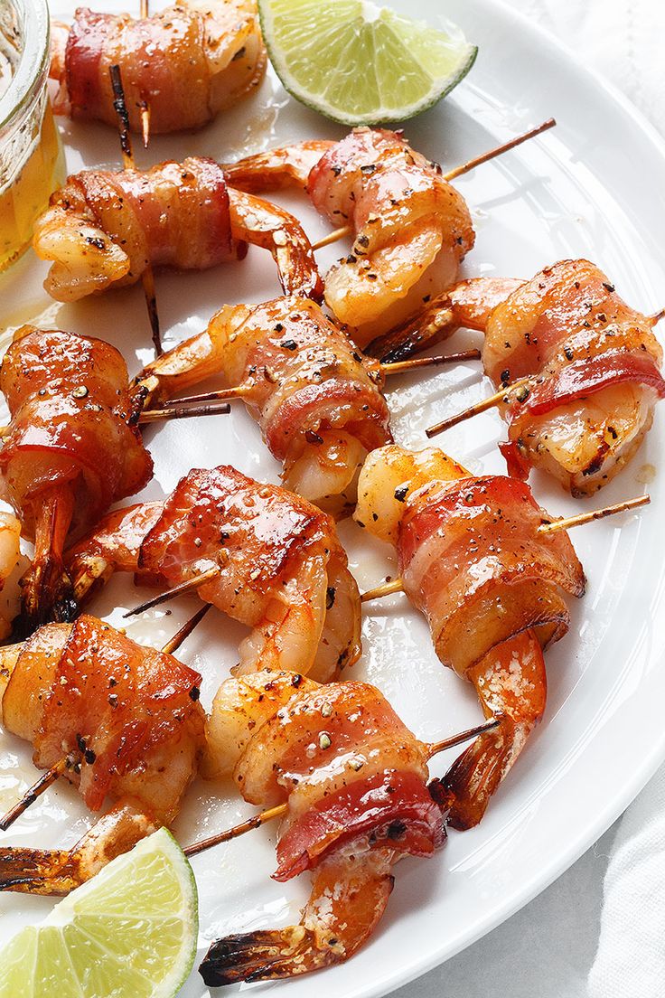 a plate with shrimp skewers, lime wedges and a small bowl of dipping sauce