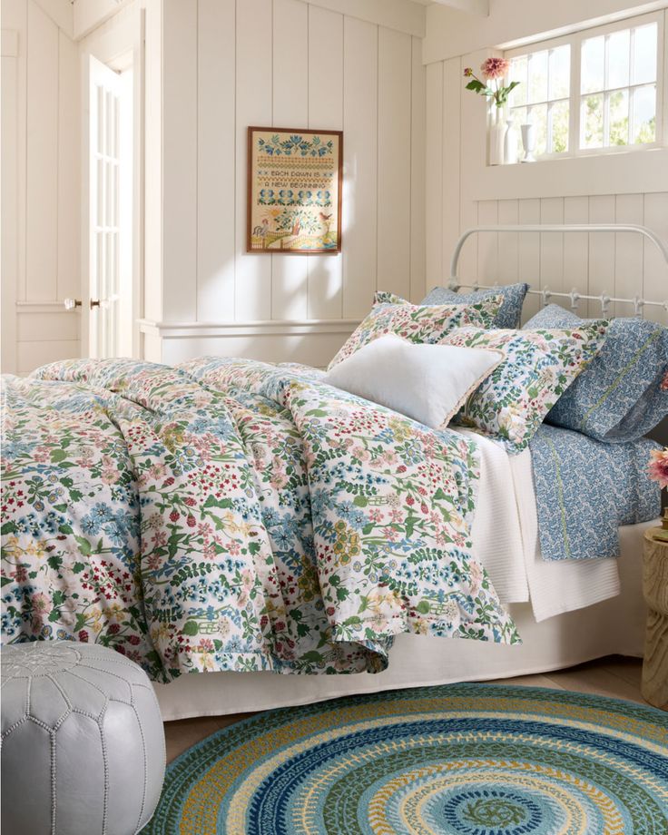 a bedroom with white walls and floral bedding, rugs on the floor and windows