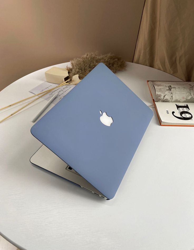 an apple laptop sitting on top of a white table next to books and a stuffed animal