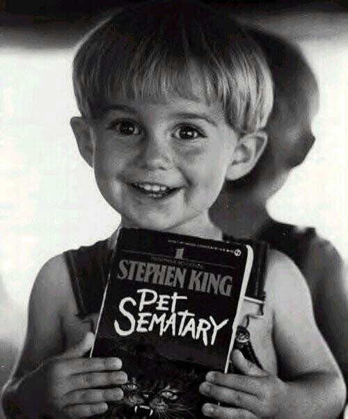 a young boy holding up a book that says stephen king pet seminary