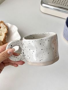 a person holding a coffee cup in front of a piece of bread on a plate