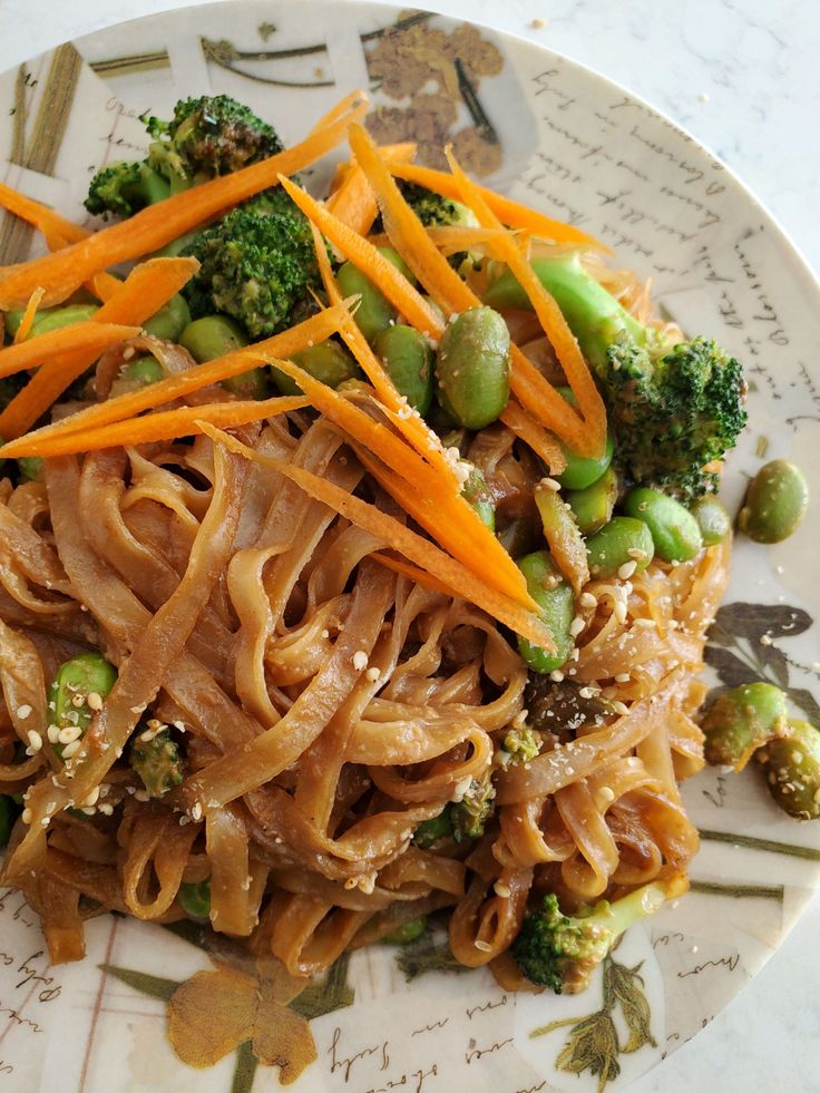 a white plate topped with pasta and veggies on top of a marble table