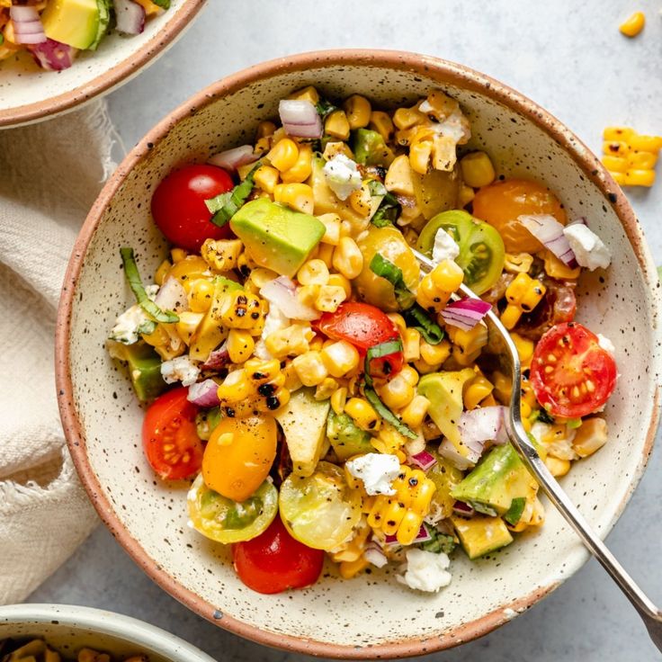 two bowls filled with different types of food on top of a white tablecloth next to other dishes and utensils