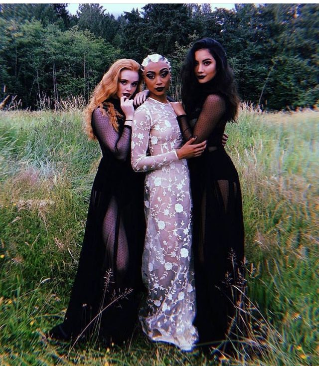 three women in black and white gowns posing for a photo with trees in the background