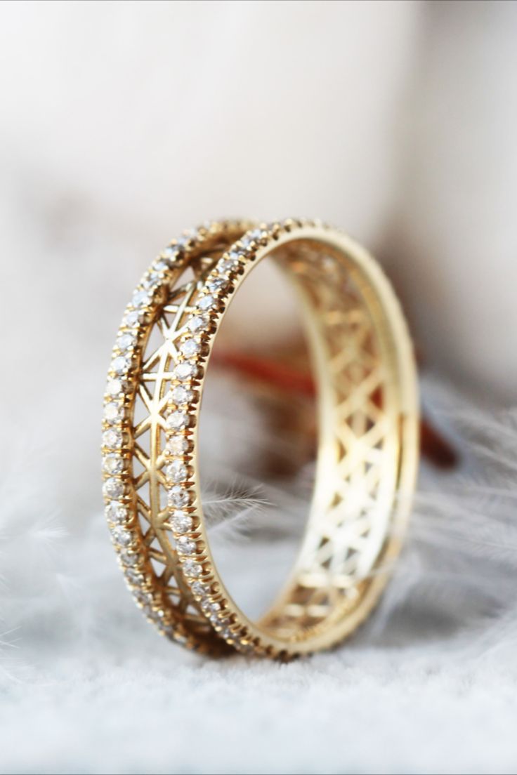 two gold rings with diamonds on them sitting on a feathery white surface in front of a blurry background