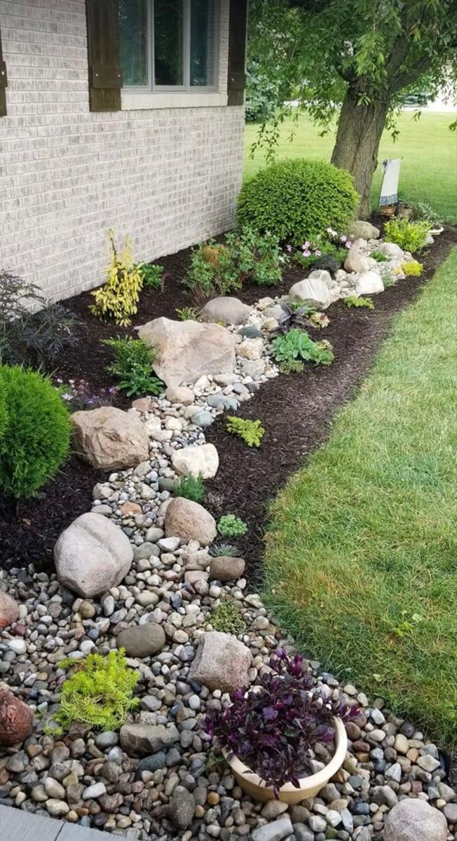 a garden with rocks and plants in front of a house