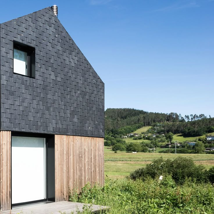 a black house with a white door in the middle of a grassy field next to trees