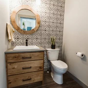 a white toilet sitting next to a wooden cabinet in a bathroom under a round mirror