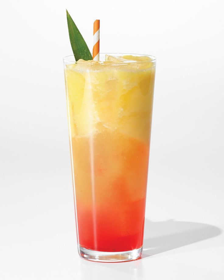 an orange and yellow drink in a tall glass with a green leaf sticking out of it