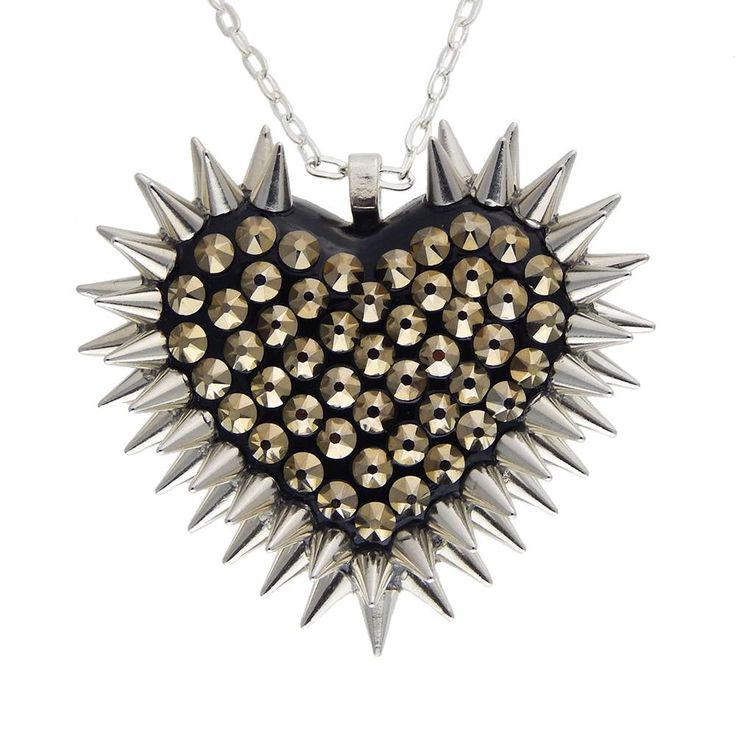 Crafted with care in our Cleveland studio, this iconic pendant features a striking spiked heart design and dozens of hand placed metallic champagne-gold crystals. DETAILS Heart Charm: 2" wide Chain: 18" chain THE COLOR Inspired by the mineral of the same name, Pyrite is a warm, champagne gold hue that adds a touch of luxury and sophistication to any outfit. SIZE CHART Silver Heart Jewelry With Ball Chain, Silver Heart-shaped Ball Chain Jewelry, Silver Heart-shaped Punk Jewelry, Punk Style Heart Pendant Jewelry With Heart Charm, Edgy Spiked Jewelry For Parties, Edgy Silver Jewelry With Spikes, Edgy Silver Jewelry With Heart Charm, Edgy Heart-shaped Silver Jewelry, Edgy Silver Heart-shaped Jewelry