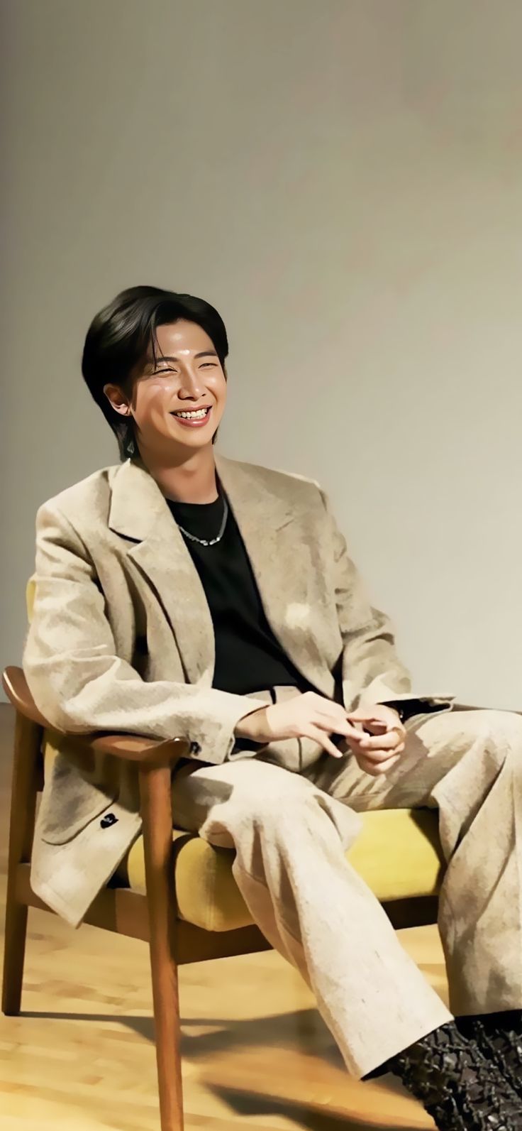 a man sitting in a chair with his legs crossed, smiling at the camera while wearing glasses