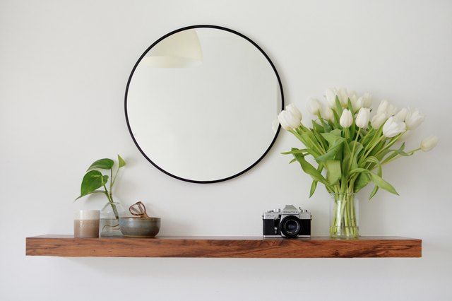 a vase with flowers and a mirror on the wall above it next to a camera