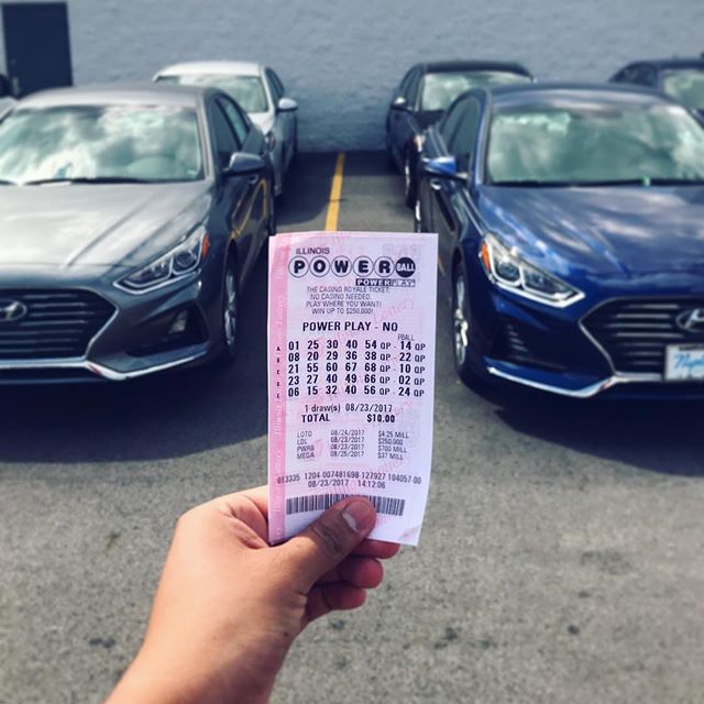 a person holding up a powerball ticket in front of two parked cars