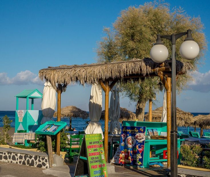 an outdoor seating area next to the ocean with tiki huts and umbrellas