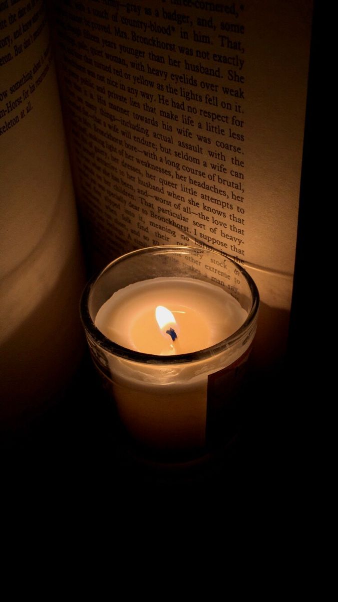 a lit candle sitting next to an open book