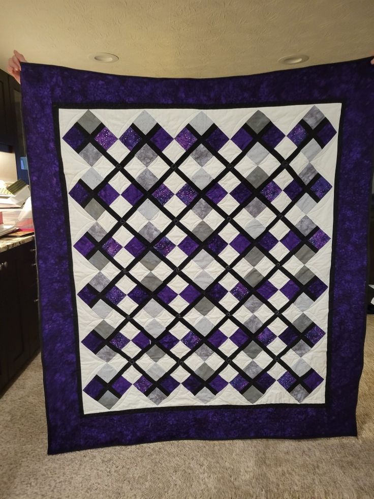 a purple and black quilt hanging on the wall