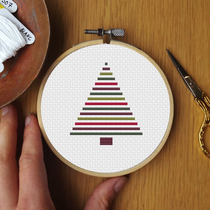 a hand is holding a cross stitch christmas tree ornament next to scissors and yarn