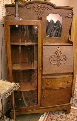 an old wooden china cabinet with glass doors and carvings on the front, next to a small table