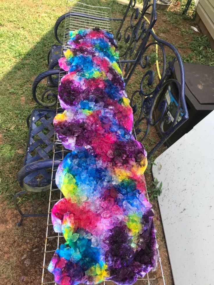 a colorful blanket is sitting on a metal bench in the grass next to a white table