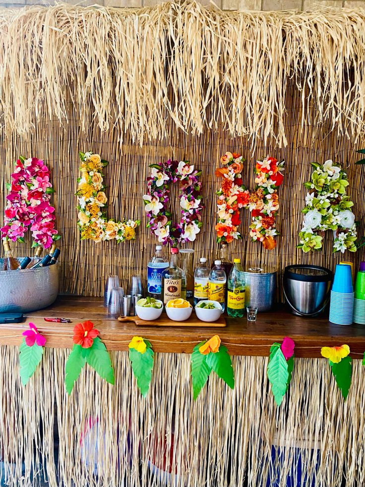 a table topped with lots of flowers next to a wall covered in tiki grass