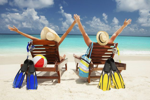 two people sitting in chairs on the beach with their arms up and hands raised above their heads