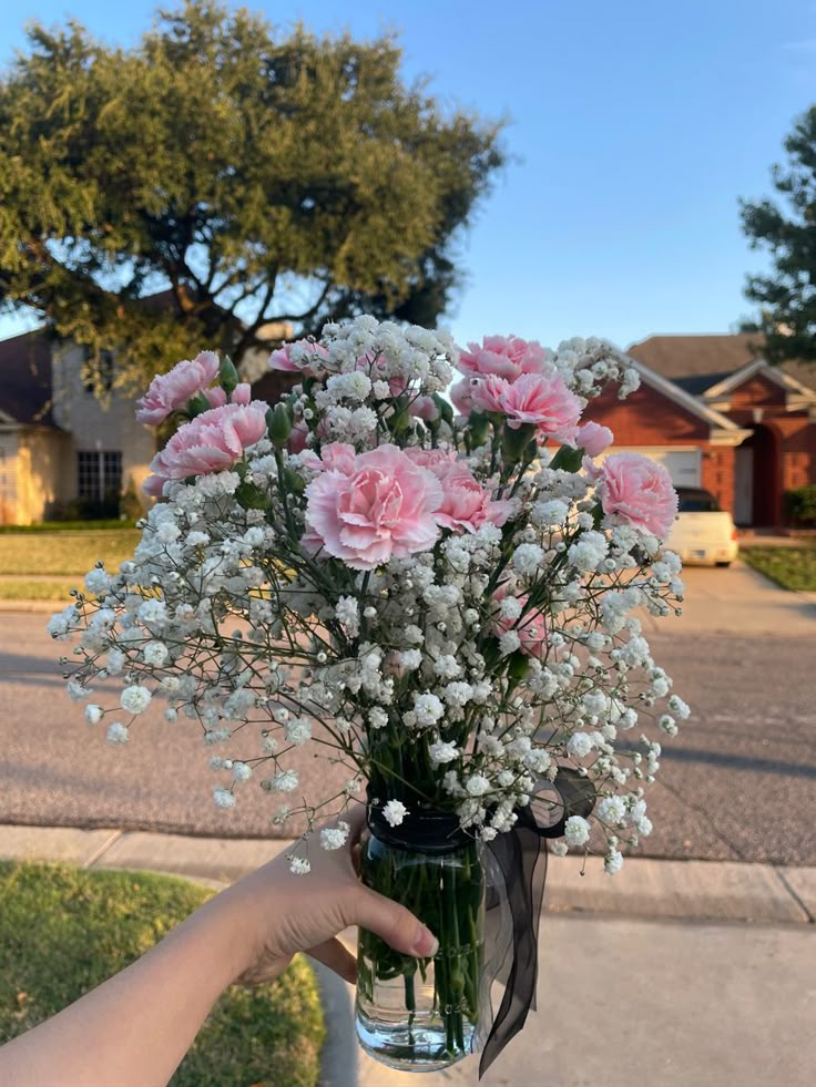 a person holding a vase with flowers in it on the side of a road near some houses